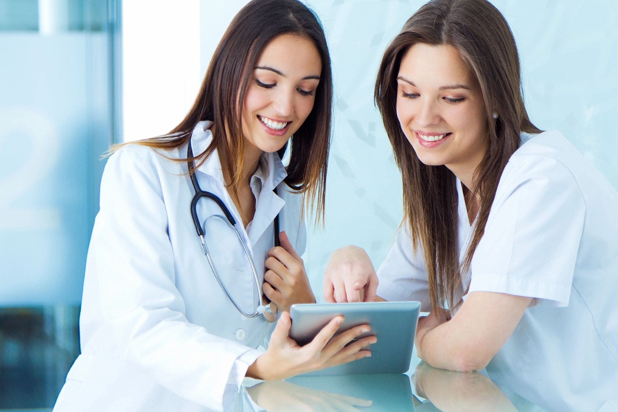 Two women in lab coats looking at a tablet.