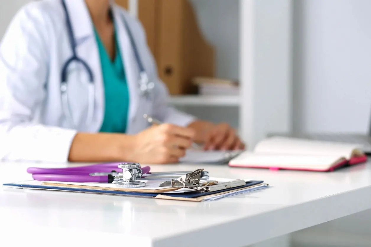 A doctor sitting at the table with papers and clipboard.